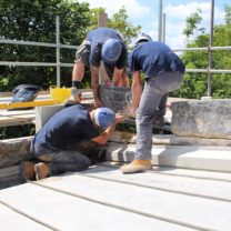 Image showing three of our stonemasons lifting existing stone onto newly carved and installed bases of the battlement stones